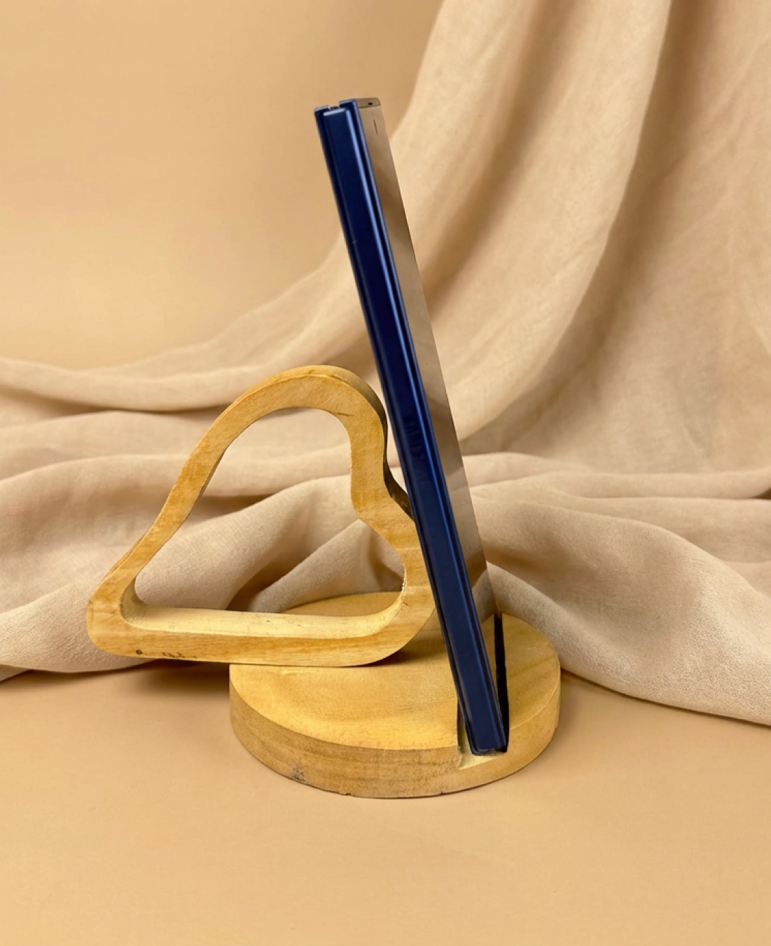 Handcrafted wooden heart-shaped phone stand holding a smartphone on a natural wooden base