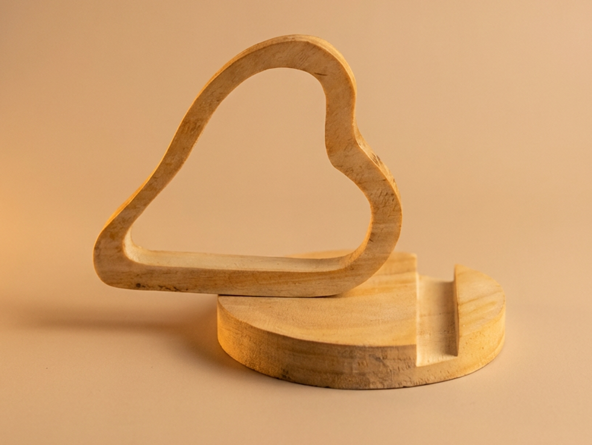 Handcrafted wooden heart-shaped phone stand holding a smartphone on a natural wooden base
