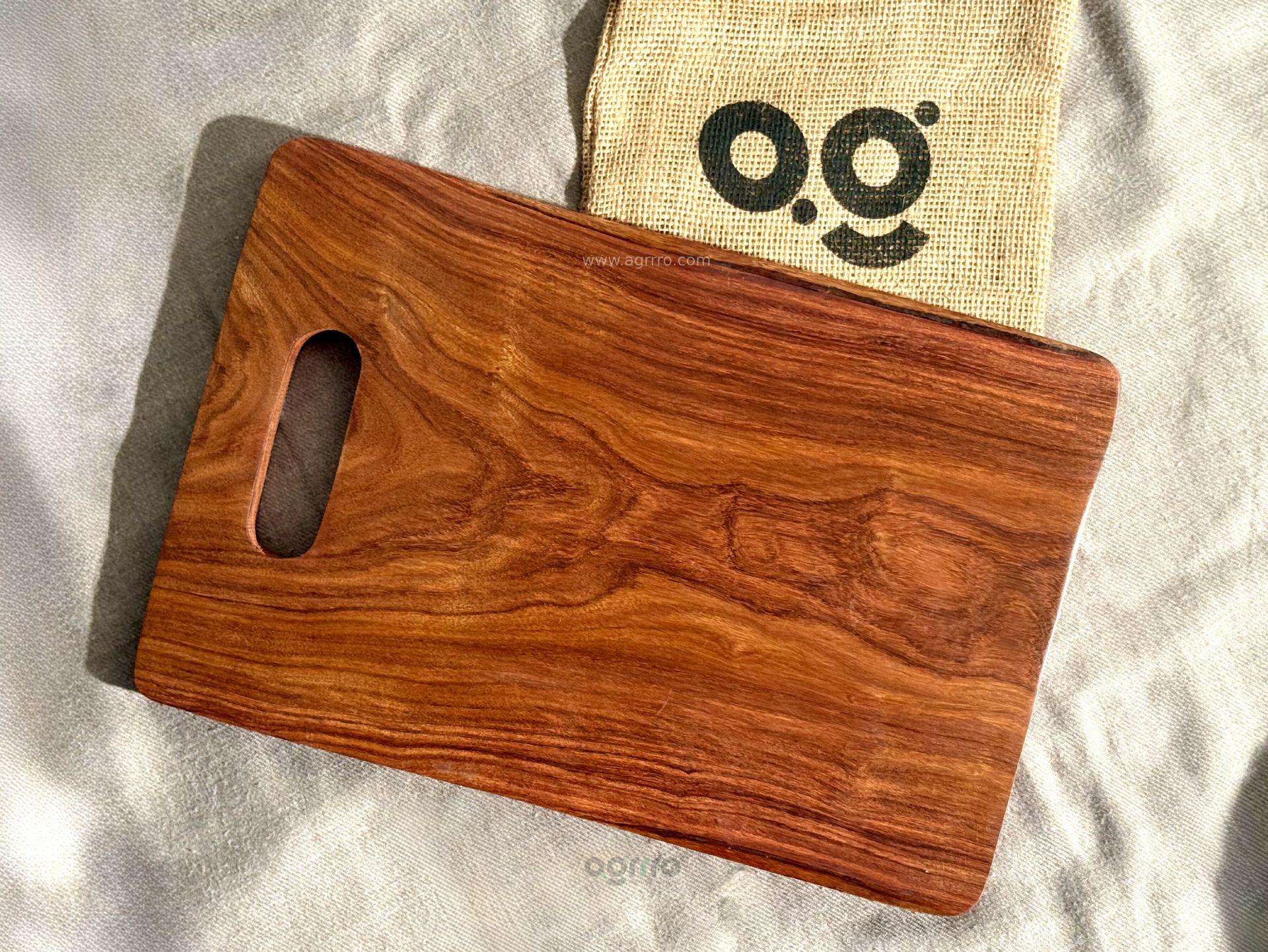 A clean top-down view of an empty rectangular Sheesham wood chopping board with visible natural grain, placed on a linen cloth next to a jute bag with the Agrrro logo.