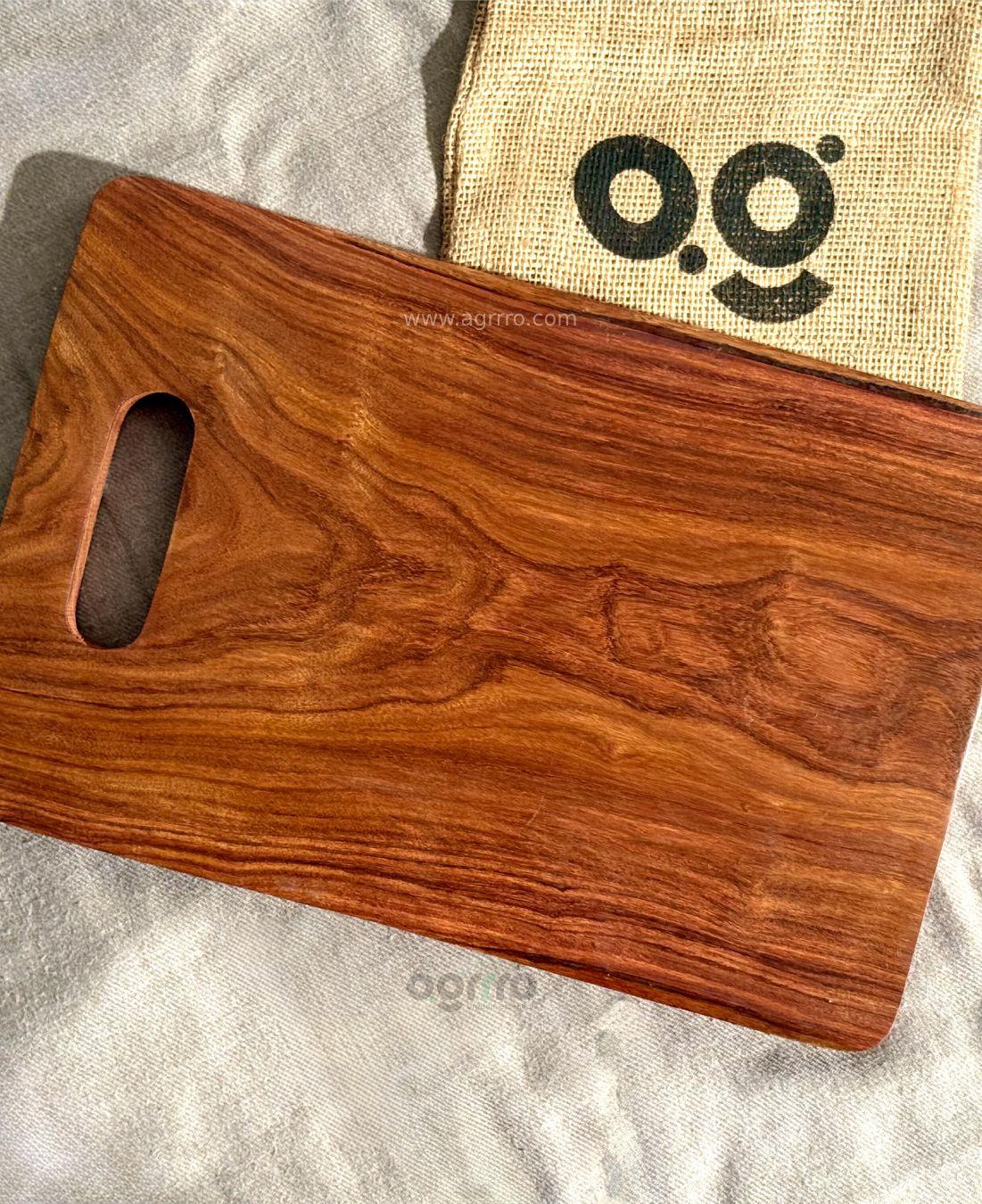 A clean top-down view of an empty rectangular Sheesham wood chopping board with visible natural grain, placed on a linen cloth next to a jute bag with the Agrrro logo.